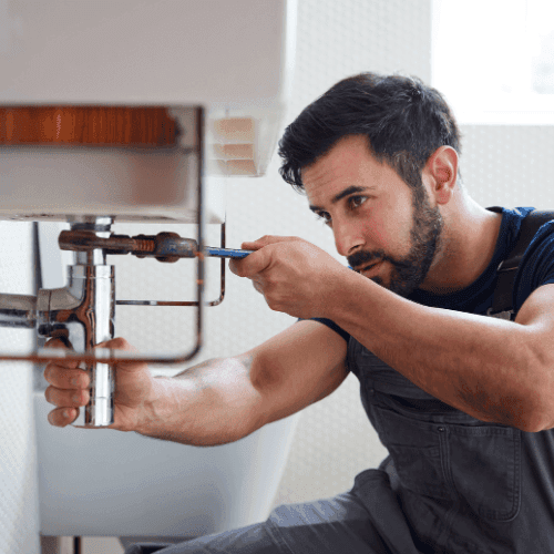 Professional plumber working on pipes under sink